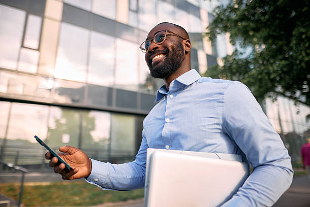 istock Smiling businessman walking and using smartphone in front of office building 2213659331