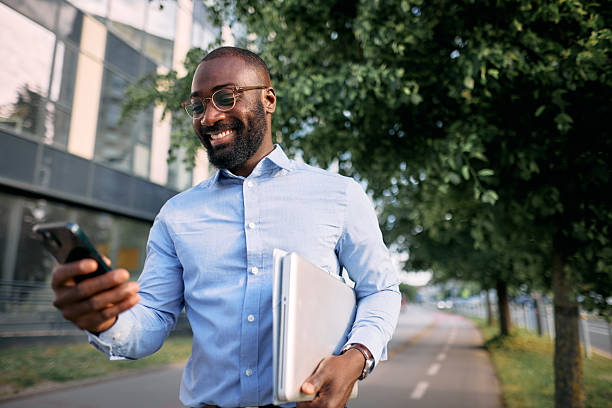 istock Smiling businessman walking and using smartphone in the city 2213659332