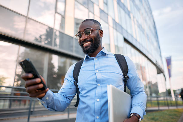 istock Smiling businessman walking and using smartphone in front of office building 2213659346
