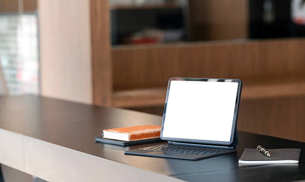Laptop showing a blank screen is placed on a kitchen table next to a bowl of fresh fruit and jars of cereals