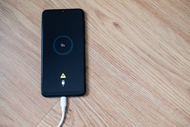 istock White charging cable plugged into smartphone displaying 0% battery on wooden table, emphasizing urgent need for power in modern life. Essential connection for daily communication 2213664294