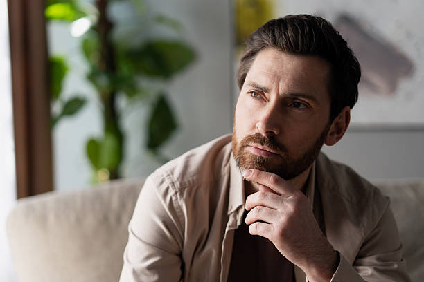 istock Pensive man thinking and looking away while sitting on sofa at home 2213665468