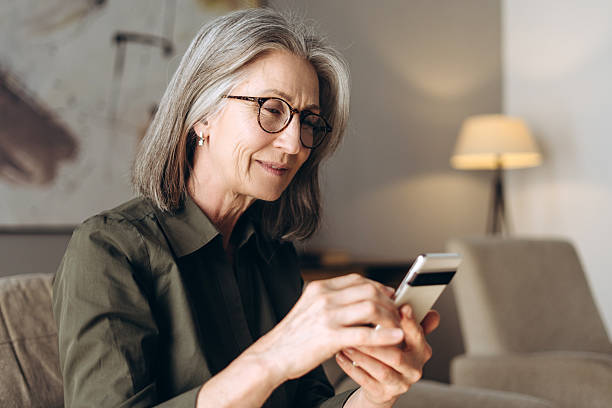 istock Senior woman using mobile phone at home sitting on sofa 2213665545