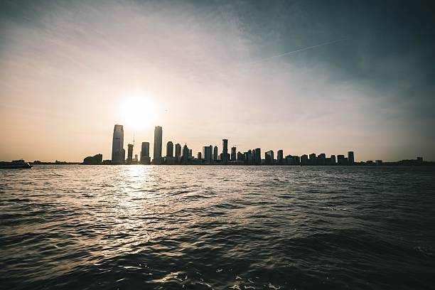 Silhouette of a city skyline at sunset with a calm river in the foreground, showcasing urban architecture against a golden sky.