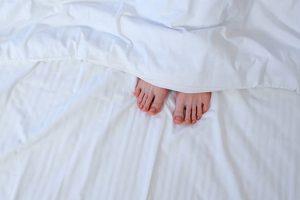 istock Woman's moving feet hiding it under the blanket in bed among white linen. 2213671299