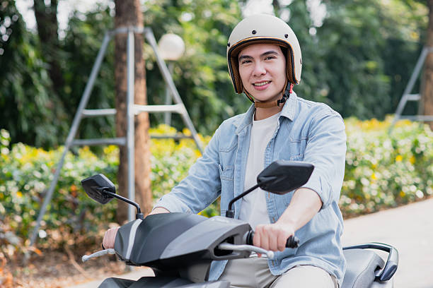 istock Young man riding a scooter with a helmet in a sunny park setting surrounded by greenery 2213671509
