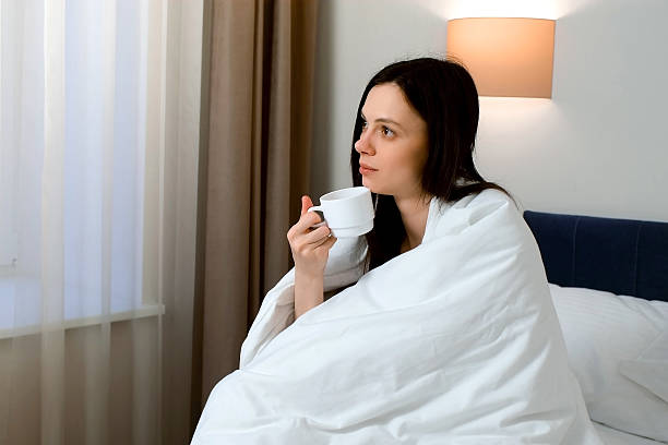 istock Thoughtful sleepy young woman wrapped in whate blanket is drinking tea. 2213672052