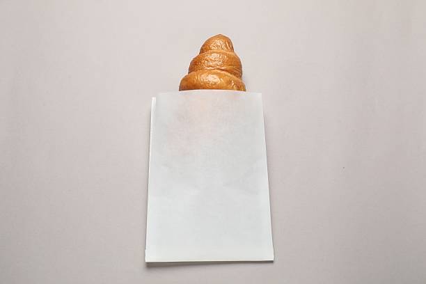 Paper bag with fresh croissant on beige background, top view