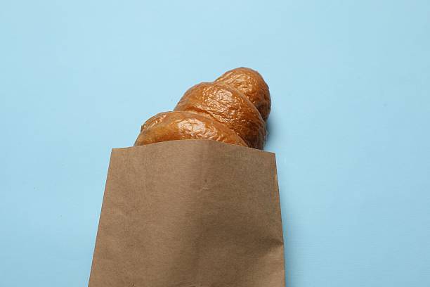 Paper bag with fresh croissant on light blue background, above view