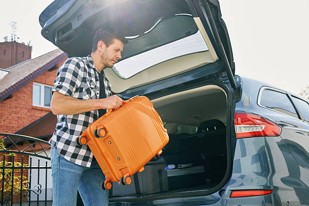 istock Man loading suitcase into car trunk, Packing luggage for travel 2213672530