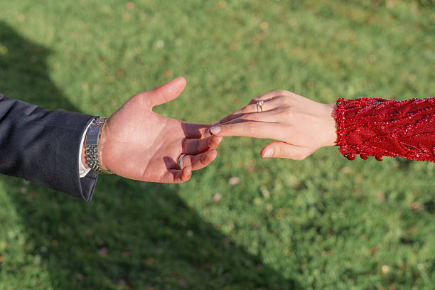 Hands of a couple reaching towards each other symbolizing connection and commitment. A woman wearing a red dress shows an engagement ring as they connect outdoors.