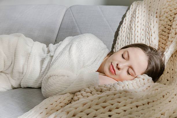istock Peaceful young woman sleeping on cozy sofa in soft white pajamas 2213673639
