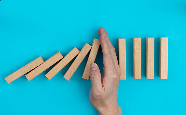 istock Man hand stopping the dominos falling 2213673898