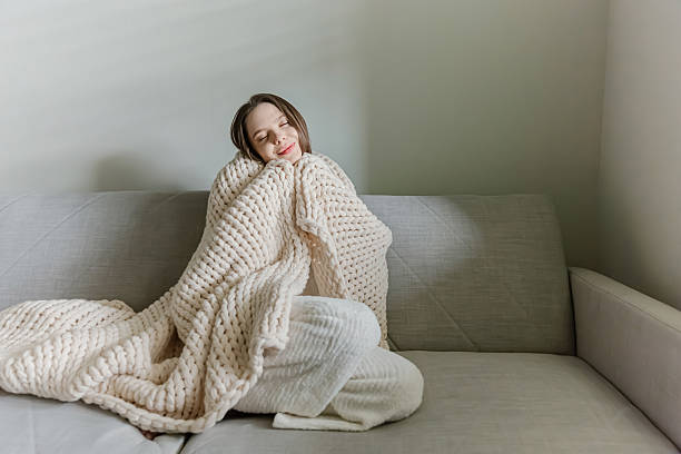 istock Woman wrapped in chunky knit blanket sitting on sofa 2213673993