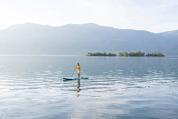 istock Man Paddleboarding on Serene Lake with Mountain View 2213674899