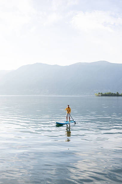 istock Man Paddleboarding on Serene Lake with Mountain View 2213674938