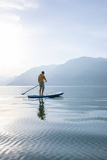 istock Man Paddleboarding on Serene Lake at Sunrise 2213675095