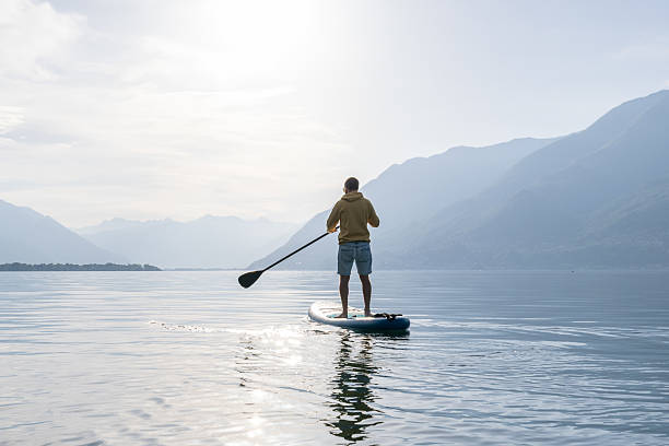 istock Person Paddleboarding on Serene Mountain Lake at Sunrise 2213675413