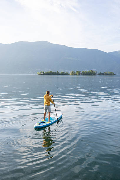 istock Man Paddleboarding on Serene Lake with Mountain View 2213678438