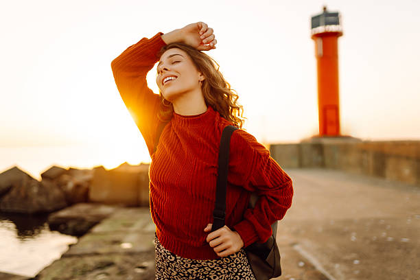 istock A happy woman with a backpack feels free on a pier overlooking a lighthouse. 2213678509