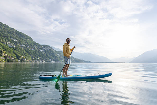istock Man Paddleboarding on Serene Lake Surrounded by Mountains 2213678580