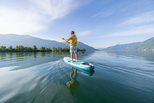 Man paddleboarding on calm lake with mountains in background. Outdoor adventure in stunning natural landscape. Peaceful recreation on water for nature enthusiasts.