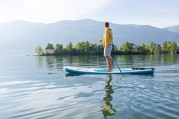 istock Man Paddleboarding on Serene Lake with Mountain Views 2213678699