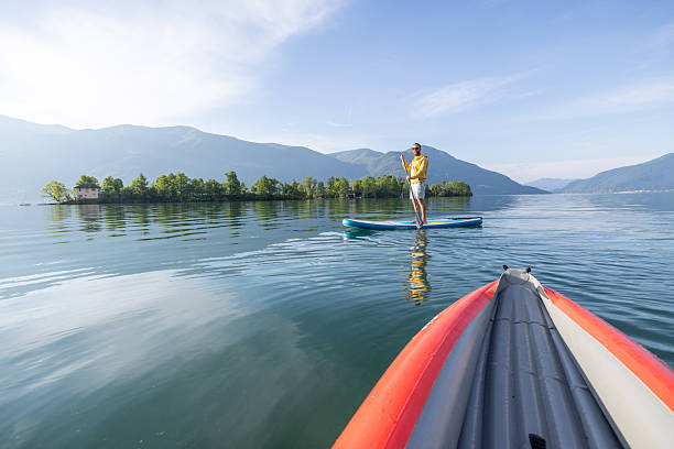 Man in yellow jacket paddleboarding on calm lake, surrounded by scenic mountains. Tranquil outdoor adventure and lake activity in peaceful natural setting.