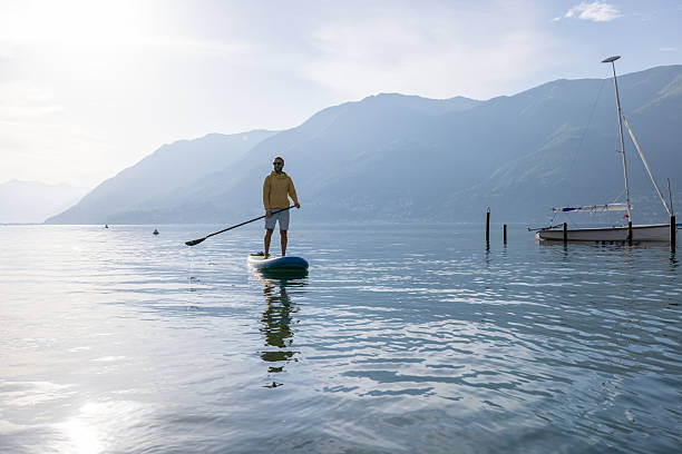 istock Man Paddleboarding on Serene Lake with Mountain Views 2213679174