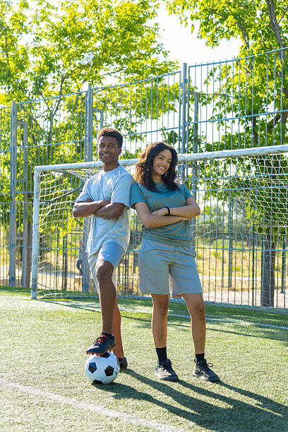Two young soccer players standing on a field with their arms crossed, one foot resting on a soccer ball, exuding confidence and teamwork
