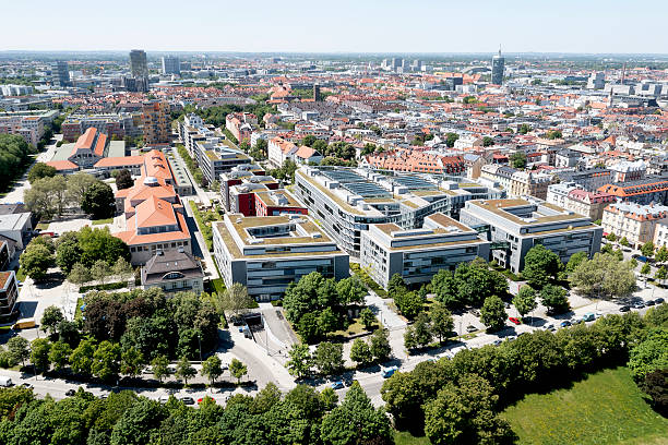 Aerial view of Munich downtown district with residential and office buildings, shopping malls, streets and green areas under blue sky in summer.