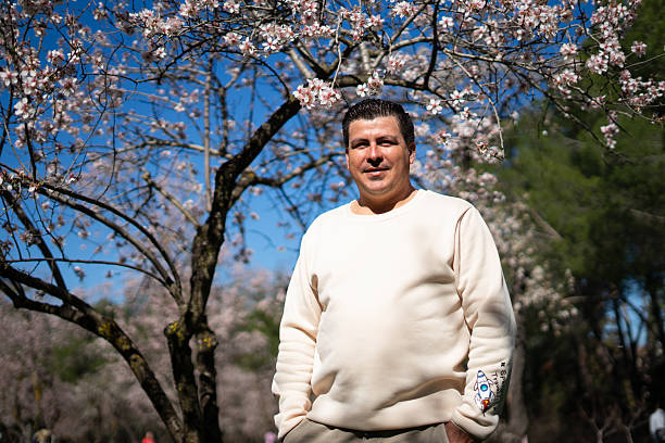 Latin farmer smiling under a blooming almond tree in a spring orchard