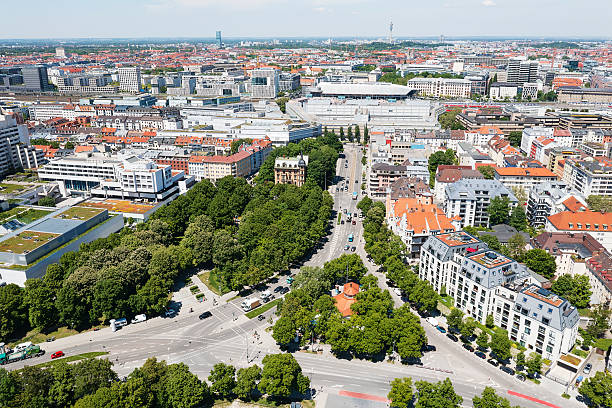 Aerial view of Munich downtown district with residential buildings, shopping malls, streets and green areas under blue sky in summer.