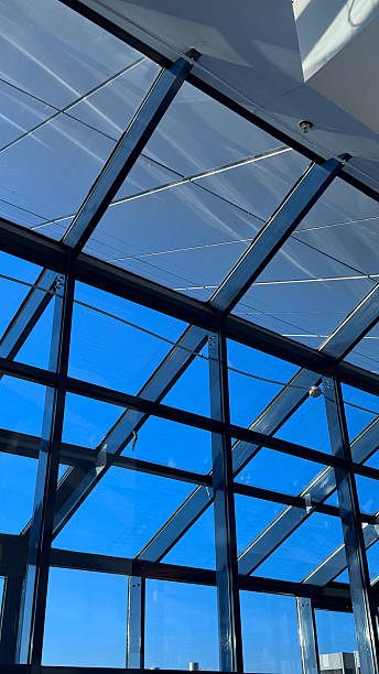 Modern architectural glass roof with blue sky backdrop creating a dynamic interplay of light and shadows in a contemporary design space