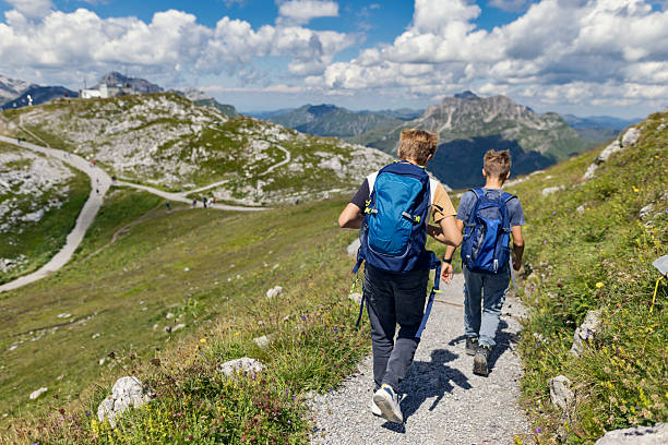 istock Two hikers trekking along a winding mountain trail under a partly cloudy sky. 2213693365