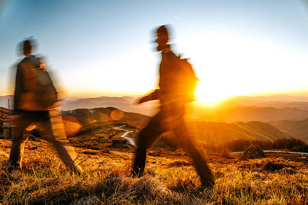 A couple walks together along a mountain path at sunset, captured in soft, blurred motion that emphasises the warmth, movement, and emotion of the golden hour adventure