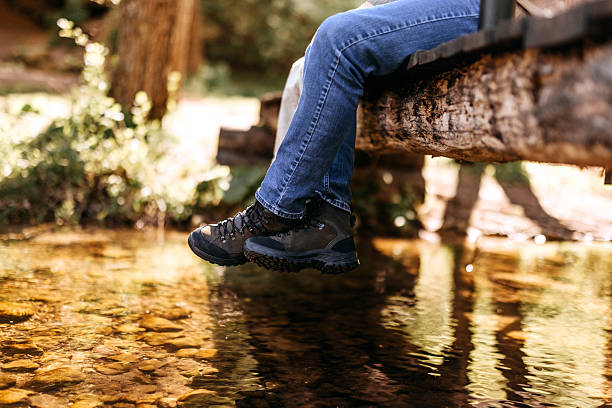Close-up shot of a hiking couple sitting side by side on a wooden bridge, only their legs and hiking boots visible, enjoying a quiet moment in the wilderness