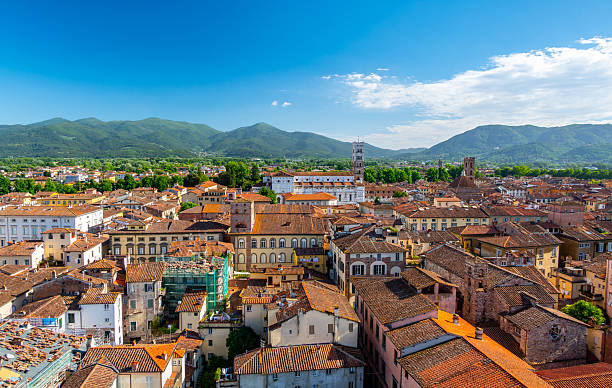 istock Panoramic view of Lucca, Italy, with red brick rooftops and historic churches seen from above. Tuscan hills and mountains form a stunning summer backdrop under a clear blue sky. 2213704719