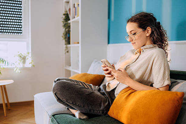 istock Casually dressed woman using smartphone while sitting on a sofa at home 2213705897