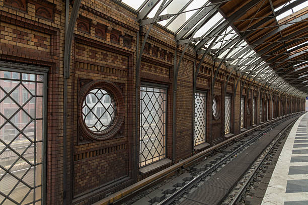 Historic urban railway station Berlin with vintage brick walls, arched roof, and patterned windows. An empty track curves through the covered platform.