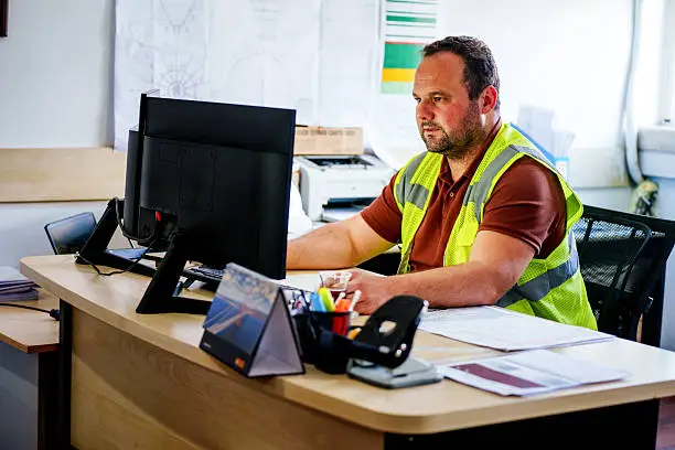Photo of Construction Site Engineer Working at Office Desk on Computer