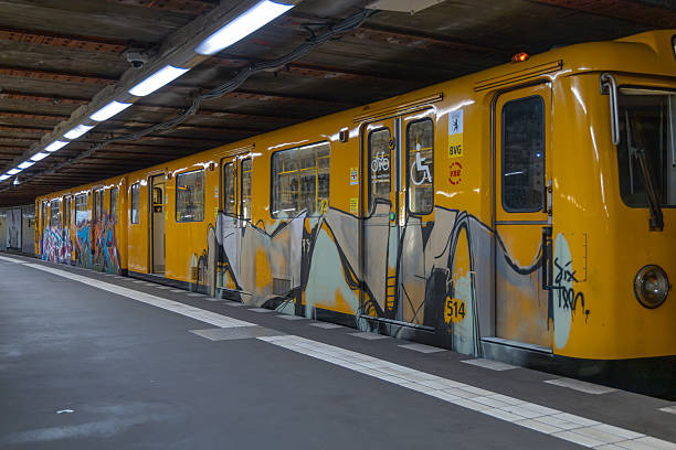 A yellow subway train car covered in vibrant graffiti art stands at a station platform with overhead lighting. Berlin, Germany. 28 March 2025.