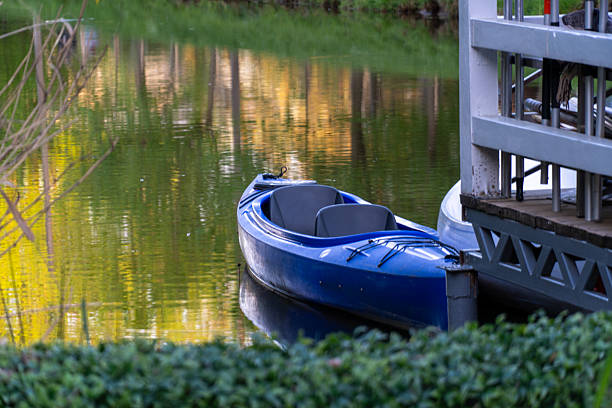 Canoe is tied to dock on a waterway with reflections of trees. Green foliage adds to the serene, natural ambiance.