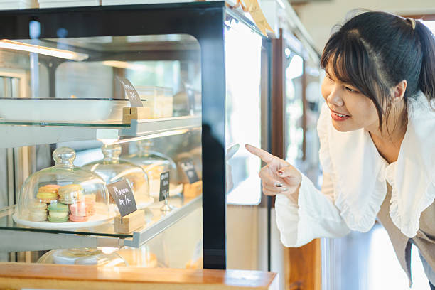 istock Asian woman working remotely as digital nomad happily points at desserts in bakery display case while enjoying her remote working day 2213708439