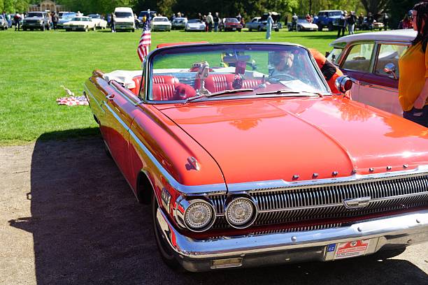 sychrov, Czech Republic – April 26, 2025: A red retro convertible parked on a lawn with people and cars around