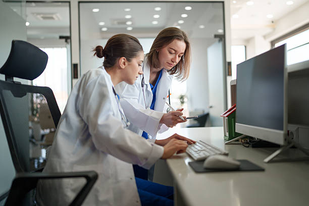istock Two Female Healthcare Workers Focused on Computer and Documents at Front Desk 2213717353