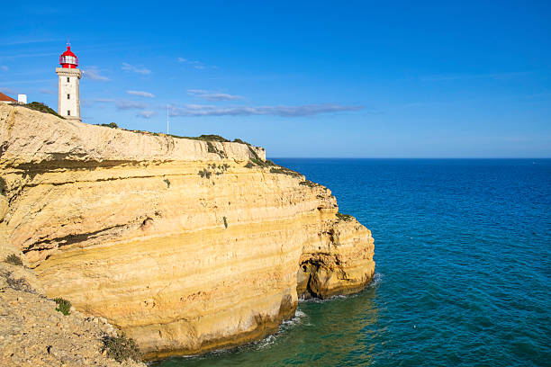 The quadrangular tower, painted in white, of the Alfanzina lighthouse stands out on a rocky promontory in the Algarve