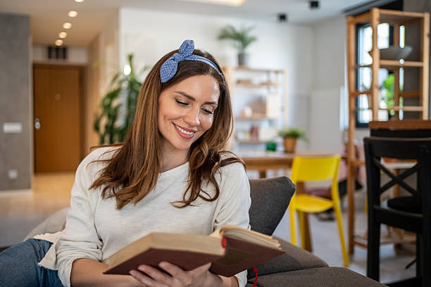 istock Young woman reading a book and smiling on sofa at home 2213720766