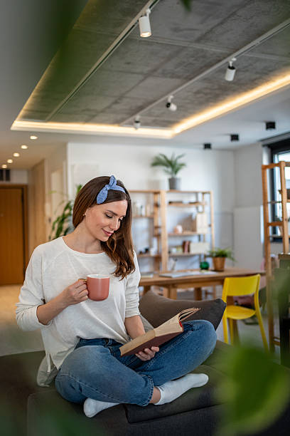 istock Young woman relaxing on sofa reading a book and drinking tea 2213721799