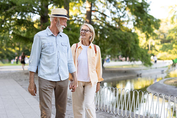 istock Senior couple walking through sunlit park by serene pond 2213726381